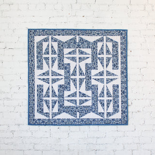 The 1751 Quilt Pattern (Download) by Millie & Bun Designs features a geometric blue and white quilt with intricate star and arrow shapes, perfect for confident beginner quilters.