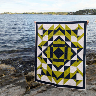 Person holding a modern geometric quilt in navy and green colors by the water, showcasing The 279 Quilt Pattern (Download) by Millie & Bun Designs.
