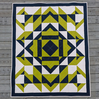 Geometric quilt in navy, olive green, and white colors displayed on wooden background, showcasing The 279 Quilt Pattern (Download) by Millie & Bun Designs.