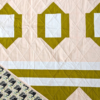Close-up of a quilt with geometric green and white blocks and beige background, showing intricate quilting by Millie & Bun Designs for The 2995 Quilt Pattern.