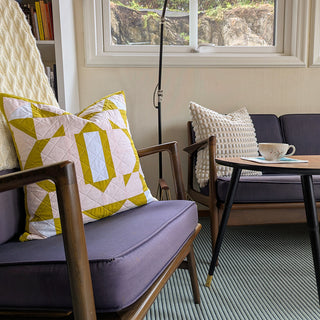 Decorative pillow featuring The 2995 Quilt Quilt Pattern (Download) by Millie & Bun Designs, displayed on a purple cushioned wooden armchair in a cozy living room setting.
