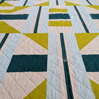 Close-up view of a modern geometric quilt with green, blue, and pink shapes, showcasing detailed quilting. The 3895 Quilt Pattern (Download) by Millie & Bun Designs.