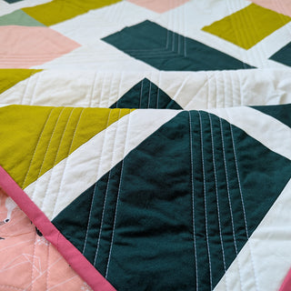Close-up of a colorful quilt with geometric shapes and detailed stitching made using The 5720 Quilt Pattern (Download) by Millie & Bun Designs.