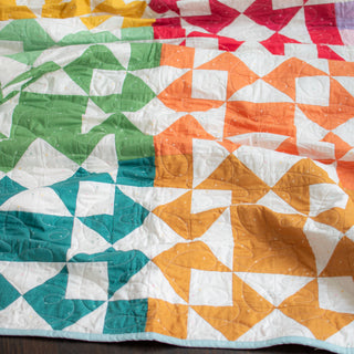 Close-up of a colorful quilt showcasing geometric patterns in shades of teal, green, orange, mustard, and red, made using the Afterglow 2.0 Quilt Pattern (Download) by Sewspicious.