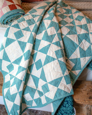 Close-up of a teal and cream geometric quilt made using the Afterglow Quilt Pattern (Download) by Sewspicious, displayed folded on a wooden surface.