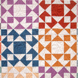 Close-up of a colorful quilt with geometric patterns featuring purple, red, blue, and orange tones, showcasing the Afterglow Quilt Pattern (Download) by Sewspicious.