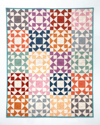 Colorful geometric quilt made with various shades of blue, orange, pink, purple, and green squares, showcasing the Afterglow Quilt Pattern (Download) by Sewspicious.