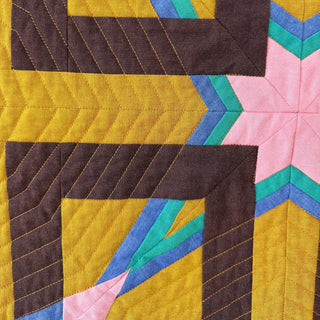 Close-up of colorful geometric quilt block featuring brown, yellow, pink, teal, and blue fabrics with detailed stitching, from Julia Wachs Designs Alcove FPP Quilt Pattern (Download).