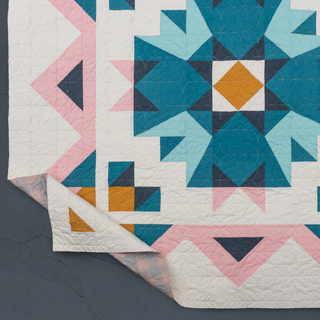 Close-up of a modern quilt corner showing geometric shapes in teal, pink, mustard, and white colors, featuring detailed quilting stitches by Toad & Sew using the Aria Quilt Pattern (Download).