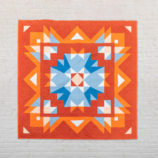 Colorful Aria quilt by Toad & Sew with orange, blue, and white patterns on a light gray background