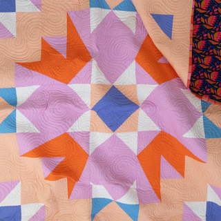 Close-up of a colorful quilt with geometric shapes in orange, purple, blue, and peach hues, showcasing the Aria Quilt Pattern (Download) by Toad & Sew.
