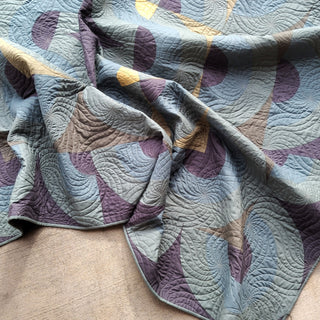 Soft textured quilt with geometric shapes in muted blues, purples, and yellows, featuring intricate quilting details, showcasing Urban Dwell Studio's Vault Quilt Pattern (Download).