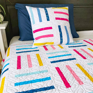 Modern quilt and pillow set featuring colorful rail fence stripe blocks in blue, pink, yellow, and teal on white, made using Bar Code Quilt Pattern (Download) by Penny Spool Quilts.