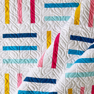 Close-up of a colorful modern quilt with geometric stripes in blue, yellow, red, and pink tones, quilted with a swirling pattern, showcasing Bar Code Quilt Pattern (Download) by Penny Spool Quilts.