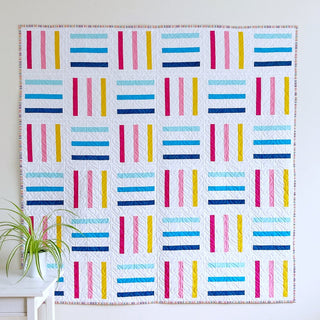 A colorful modern quilt featuring horizontal and vertical strips in blue, pink, and yellow on white, showcasing the Bar Code Quilt Pattern (Download) by Penny Spool Quilts.