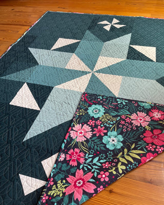 Close-up of a geometric star quilt with teal and cream tones and a floral backing, showcasing the Black Balsam Quilt Pattern (Download) by Hampton Quilt Studio.