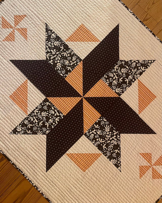 Close-up of a handmade quilt featuring a geometric star pattern in black, white, and orange fabrics, showcasing the Black Balsam Quilt Pattern (Download) from Hampton Quilt Studio.