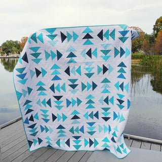Blessings Quilt Pattern (Download) by Homemade Emily Jane featuring a modern geometric quilt with turquoise, teal, navy, and white arrowlike shapes outdoors by a lake