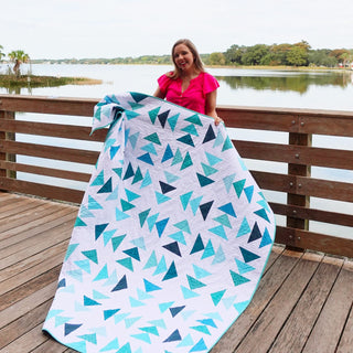 Blessings Quilt Pattern (Download) by Homemade Emily Jane featuring a woman holding a modern geometric quilt in aqua teal and navy beside a lake
