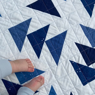 Blessings Quilt Pattern (Download) by Homemade Emily Jane featuring a modern blue and white geometric quilt with triangle blocks and a child’s feet resting on it