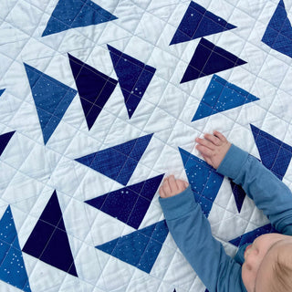 Blessings Quilt Pattern (Download) by Homemade Emily Jane featuring a blue and white geometric quilt with a child reaching across the cozy design