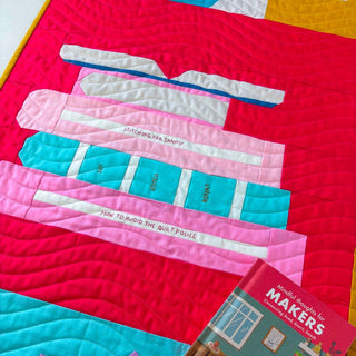 Close-up of a colorful quilt featuring stacked books with playful titles, showcasing the Book Club Block Pattern (Download) by Lou Orth Designs.