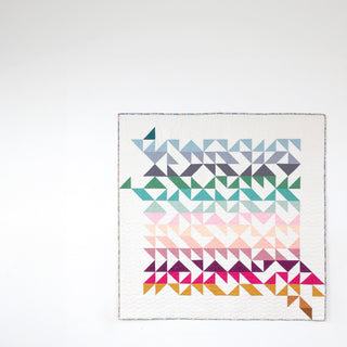 A modern quilt featuring geometric half square triangle patterns in shades of blue, green, pink, purple, and gold, designed by Lou Orth Designs using Break Away Quilt Pattern (Download).