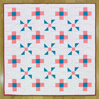 A finished quilt featuring pink and teal geometric blocks on a white background with swirling quilting details, made using the Breezy Shores Quilt Pattern (Download) by Shadow Valley Quilts.