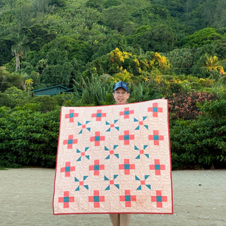 Person standing outdoors holding a colorful quilt featuring geometric blocks with coral and teal accents, showcasing the Breezy Shores Quilt Pattern (Download) by Shadow Valley Quilts.