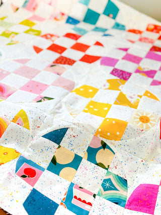 Bright close-up of a colorful patchwork quilt made with varied patterned fabrics, showcasing intricate stitching and the Carlita Quilt Pattern (Download) from Sewspicious.