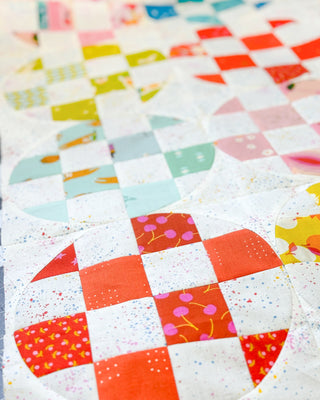 Close-up of a colorful quilt featuring bright reds, pinks, and pastel shades with a speckled white background, showcasing the detailed craftsmanship of the Carlita Quilt Pattern (Download) by Sewspicious.