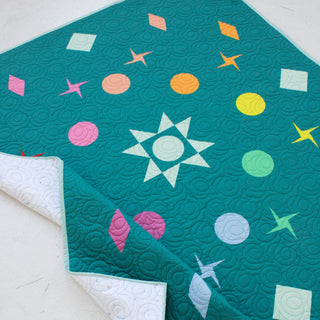 Quilt featuring vibrant star and circle shapes on a teal background with swirling stitching, showcasing the Celestial Quilt Pattern (Download) by Lou Orth Designs.