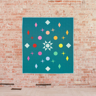 Colorful celestial-themed quilt with stars, circles, and diamond shapes on a teal background, featuring the Celestial Quilt Pattern (Download) by Lou Orth Designs.