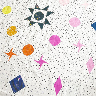 Closeup of a colorful quilt with star and geometric shapes on a white background featuring tiny black stars, showcasing the Celestial Quilt Pattern (Download) by Lou Orth Designs.