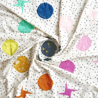 A colorful quilt featuring celestial-themed circles and stars on a white background, designed by Lou Orth Designs, showcasing the Celestial Quilt Pattern (Download).