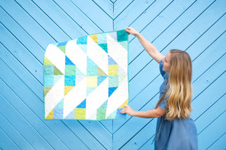 Cirrus Quilt Pattern (Download) by Homemade Emily Jane featuring a bright modern geometric quilt with white teal and lime shapes held by a woman against a blue wall