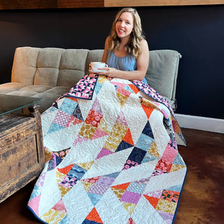 Cirrus Quilt Pattern (Download) by Homemade Emily Jane, featuring a colorful geometric quilt with flowing blocks draped over a smiling woman on a sofa
