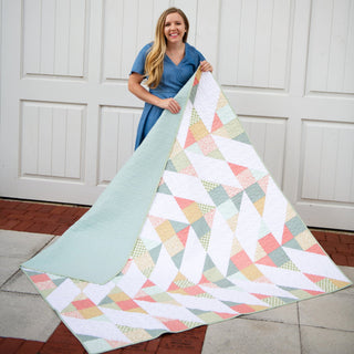 Homemade Emily Jane's Cirrus Quilt Pattern (Download) shown as a pastel geometric quilt with flowing shapes held by a smiling woman outdoors