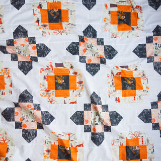 Close-up of a quilt made using bright orange, black, and cream fabrics with scenic prints, showcasing the City Lights Quilt Pattern (Download) by Lou Orth Designs.
