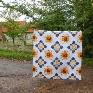 Quilt featuring bright orange, black, and white geometric blocks displayed outdoors, made using the City Lights Quilt Pattern (Download) by Lou Orth Designs.