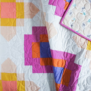 Close-up of a colorful geometric quilt made with the City Lights Quilt Pattern (Download) by Lou Orth Designs, featuring vibrant pink, orange, and blue blocks with detailed circular stitching.