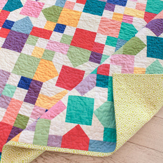 Close-up of a colorful patchwork quilt made with the Confetti Garden Quilt Pattern (Download) by Straight Stitching, featuring vibrant geometric shapes and a patterned yellow backing.