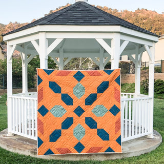 Connector Quilt Pattern (Download) by Homemade Emily Jane, a modern geometric quilt in coral orange, teal, and blue displayed on a white gazebo.