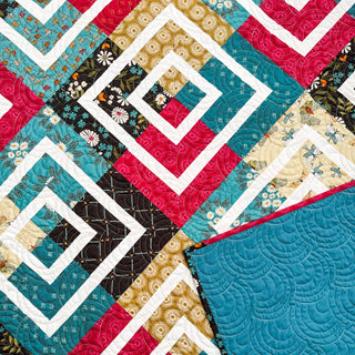 Close-up of a colorful geometric quilt pattern featuring teal, red, gold, and floral prints, showcasing the Coreina Quilt Pattern (Download) by A Piece of Quiet Quilts.
