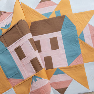 Close-up of a handmade quilt featuring geometric house blocks in soft brown, blue, pink, and yellow colors, showcasing the Cottagecore Quilt Pattern (Download) by Toad & Sew.