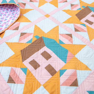 Close-up of a colorful quilt made with the Cottagecore Quilt Pattern (Download) by Toad & Sew, featuring geometric star and house blocks in warm pastel tones.