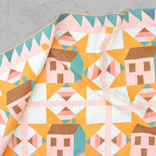 Detail of a colorful quilt featuring geometric house shapes in soft pinks, yellows, browns, and teal, showcasing the Cottagecore Quilt Pattern (Download) by Toad & Sew.