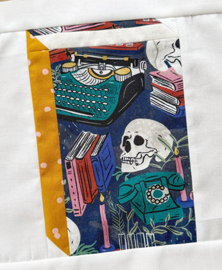 Closeup of a quilt block featuring a vintage typewriter, skull, books, and rotary phone with candles on a navy background, part of The Book Block Collection — Complete 5-Block Bundle (Download) by Lou Orth Designs.
