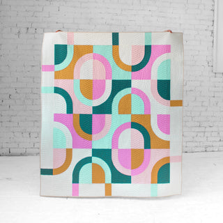 Colorful geometric Currents quilt by Eudaimonia Studio against a white brick wall