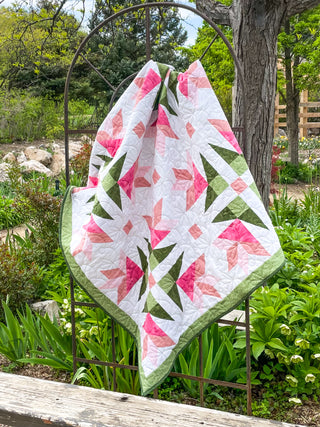 Bright floral quilt with pink and green geometric lilies draped outdoors, showcasing the Dancing Lilies Quilt Pattern (Download) by Shadow Valley Quilts.